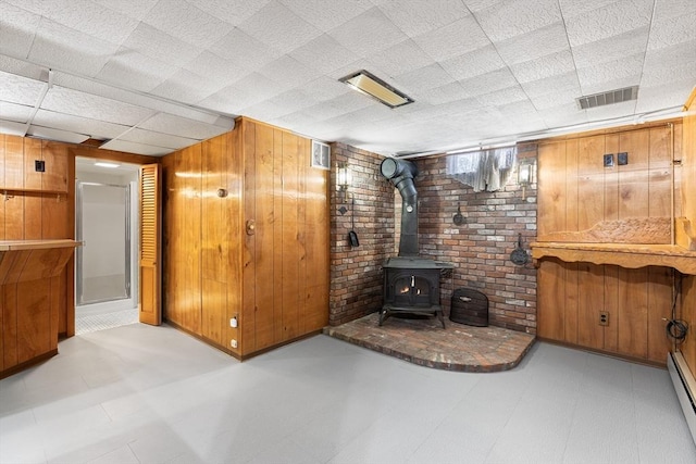 living room with a baseboard heating unit, a wood stove, and wood walls