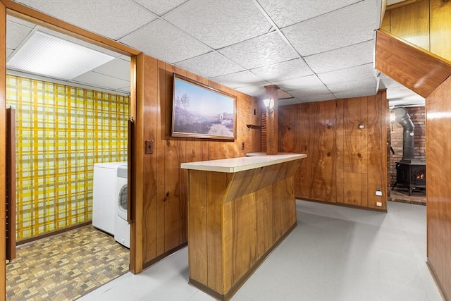 bar featuring washer / clothes dryer, wooden walls, a paneled ceiling, and a wood stove