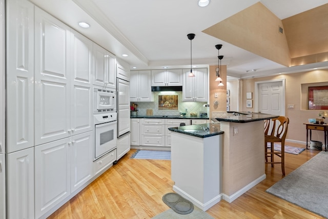 kitchen featuring light hardwood / wood-style flooring, white cabinetry, kitchen peninsula, built in appliances, and a kitchen breakfast bar