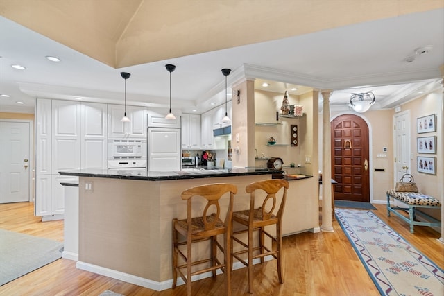 kitchen with ornamental molding, light hardwood / wood-style flooring, kitchen peninsula, a breakfast bar area, and white cabinets