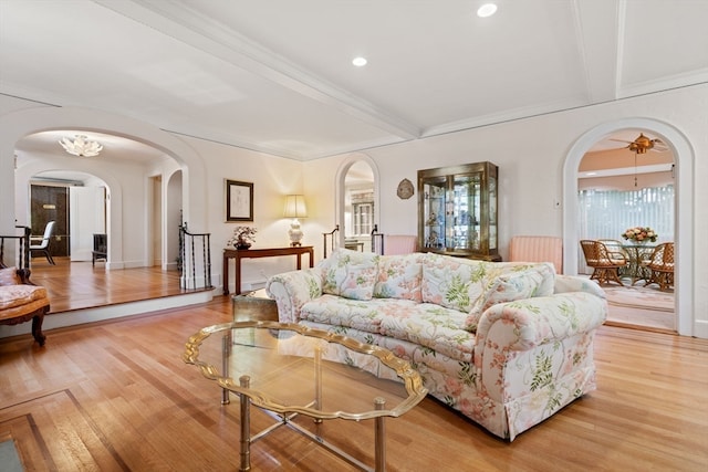 living room featuring light wood-type flooring, ornamental molding, beam ceiling, and ceiling fan