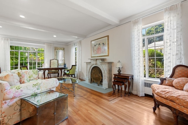 living room featuring crown molding, light hardwood / wood-style flooring, a high end fireplace, and beamed ceiling