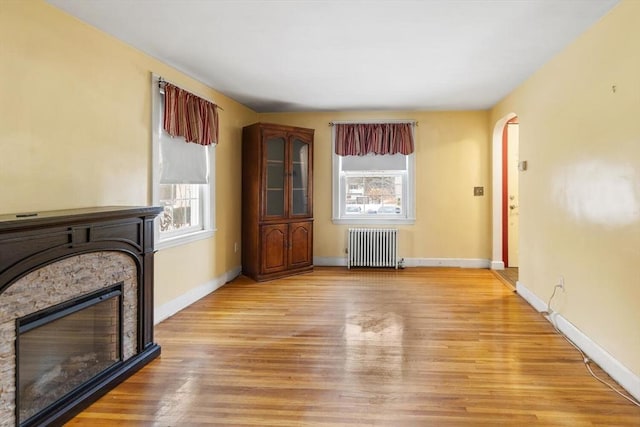 living room with light hardwood / wood-style flooring, radiator, and a stone fireplace