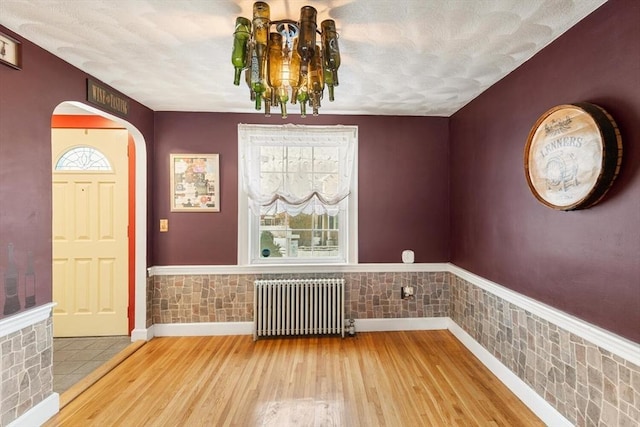 entrance foyer with wood-type flooring, radiator heating unit, and a notable chandelier