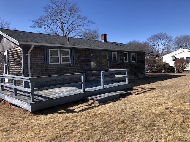 rear view of property featuring a yard, a chimney, a wooden deck, and roof with shingles