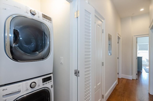 washroom featuring stacked washer / drying machine, recessed lighting, wood finished floors, laundry area, and baseboards