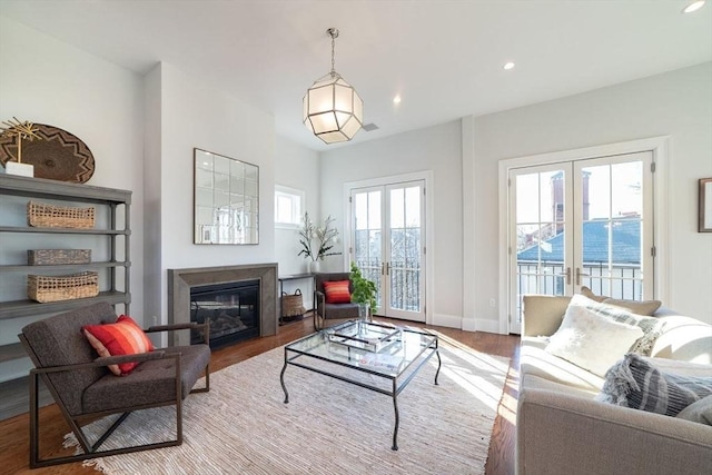 living area featuring a glass covered fireplace, wood finished floors, and french doors