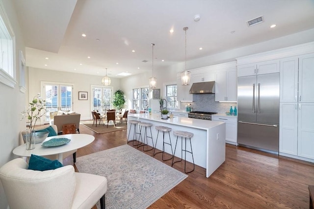 kitchen featuring a center island with sink, light countertops, visible vents, stainless steel built in refrigerator, and under cabinet range hood