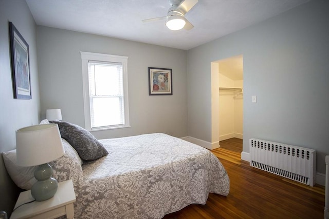 bedroom with baseboards, radiator, ceiling fan, wood finished floors, and a walk in closet