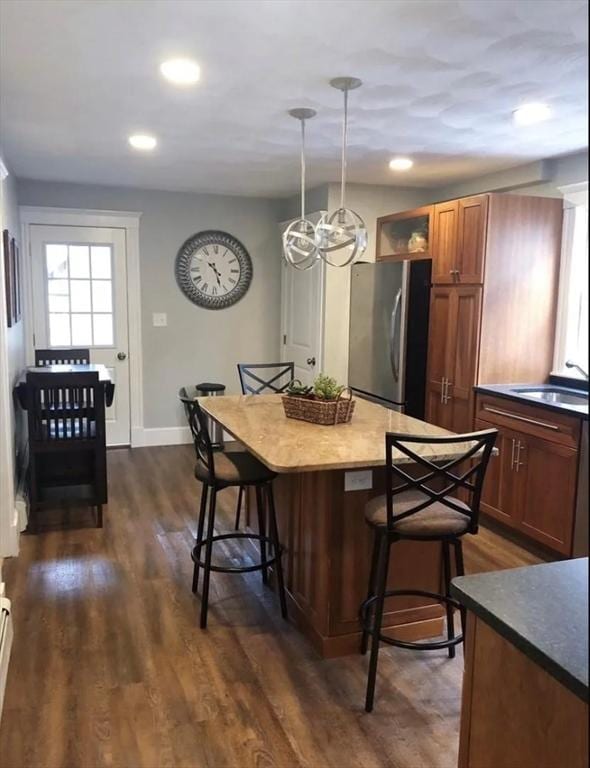 kitchen featuring a sink, a kitchen breakfast bar, freestanding refrigerator, brown cabinetry, and dark wood finished floors