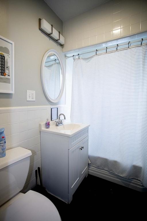 bathroom with toilet, wainscoting, tile walls, and vanity