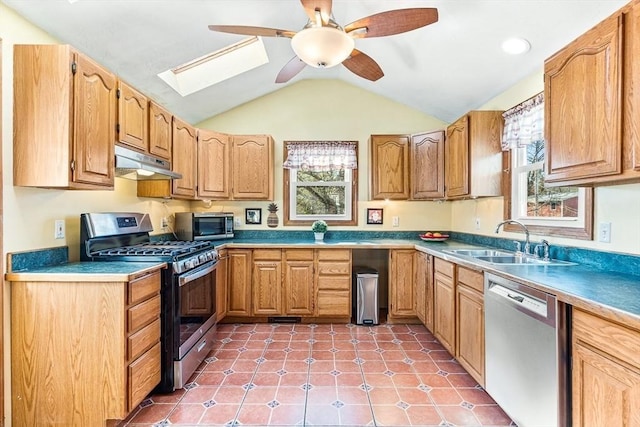 kitchen featuring vaulted ceiling with skylight, ceiling fan, a sink, under cabinet range hood, and stainless steel appliances