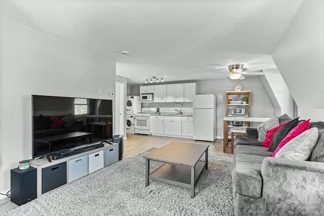 living room with stacked washing maching and dryer, light wood-style floors, a ceiling fan, and vaulted ceiling