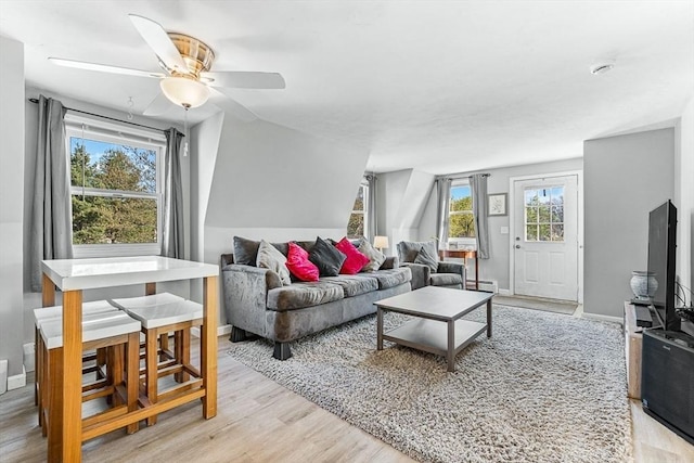 living area with baseboards, a baseboard radiator, a ceiling fan, and light wood finished floors