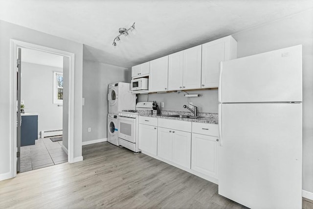 kitchen featuring stacked washer and dryer, white appliances, white cabinetry, a baseboard heating unit, and a sink