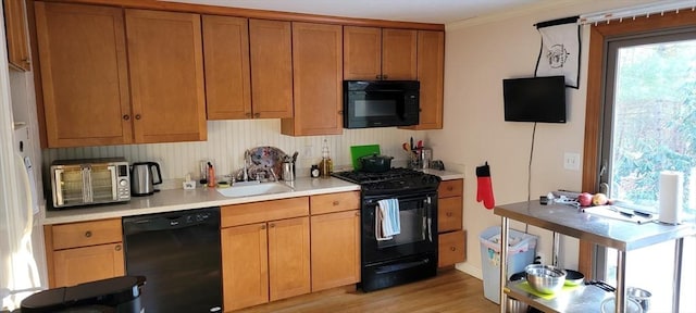 kitchen with light countertops, a sink, brown cabinetry, black appliances, and light wood-style floors