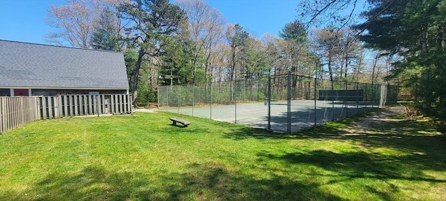 exterior space featuring a tennis court, fence, and a lawn