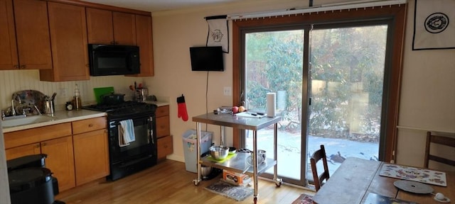 kitchen featuring light countertops, light wood-style flooring, brown cabinets, a sink, and black appliances