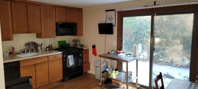 kitchen featuring light countertops, ornamental molding, a sink, black appliances, and brown cabinetry