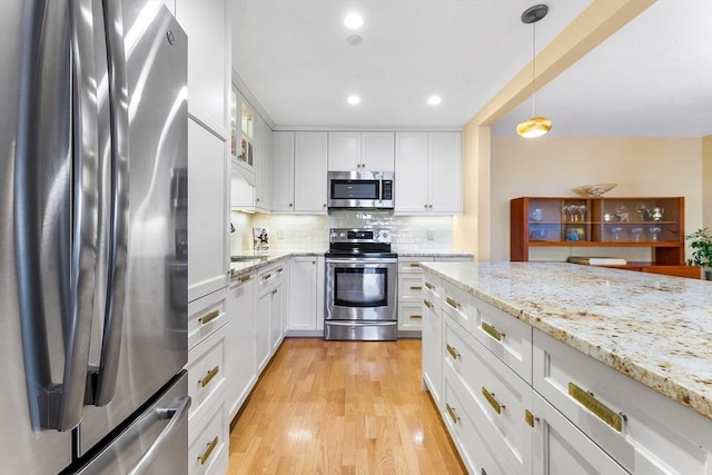 kitchen with stainless steel appliances, light stone counters, pendant lighting, decorative backsplash, and white cabinets