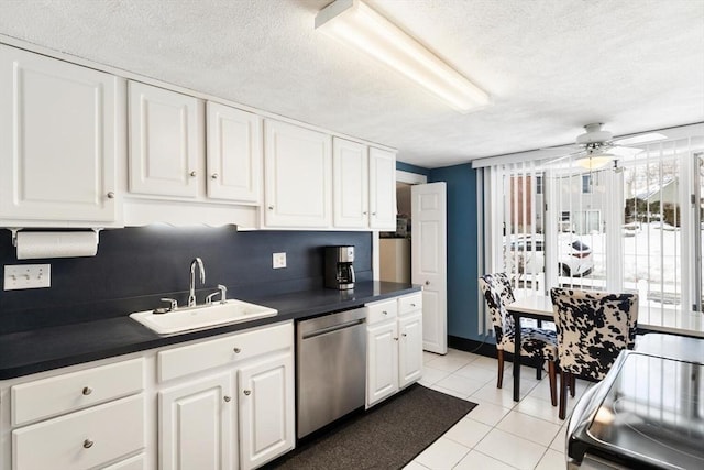 kitchen with white cabinets, dark countertops, a healthy amount of sunlight, stainless steel dishwasher, and a sink