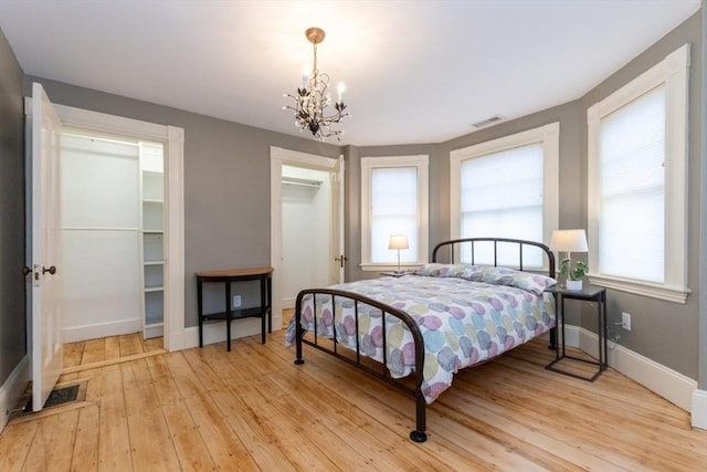 bedroom with a closet, a walk in closet, a notable chandelier, and light wood-type flooring