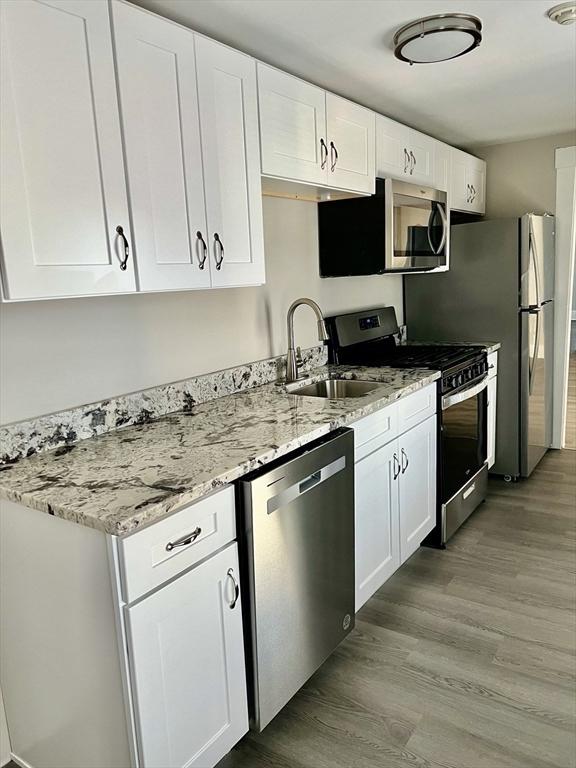 kitchen featuring light stone countertops, light wood-style flooring, white cabinets, stainless steel appliances, and a sink