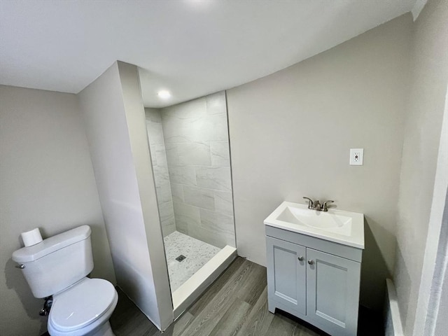 bathroom with a tile shower, toilet, vanity, and wood finished floors