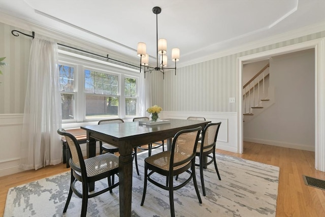 dining space with wallpapered walls, a wainscoted wall, visible vents, stairway, and a chandelier