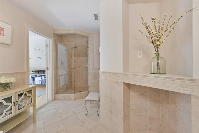 full bath featuring tile walls, visible vents, tile patterned flooring, wainscoting, and a shower stall