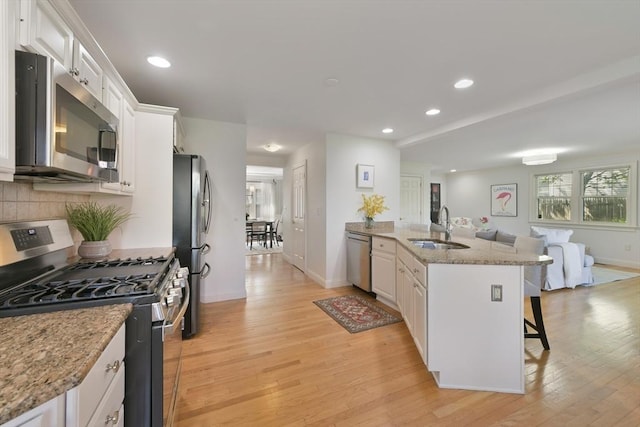 kitchen featuring light wood finished floors, a breakfast bar, a sink, stainless steel appliances, and white cabinetry