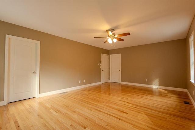 empty room with ceiling fan, light wood finished floors, visible vents, and baseboards