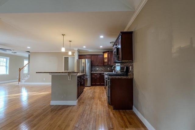 kitchen featuring light wood-style flooring, a breakfast bar area, ornamental molding, stainless steel appliances, and backsplash