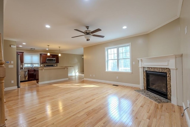 unfurnished living room featuring baseboards, ceiling fan, crown molding, light wood-type flooring, and a high end fireplace