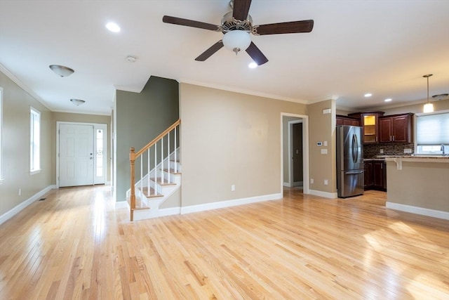 unfurnished living room with stairs, crown molding, baseboards, and light wood-style floors