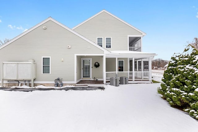 snow covered rear of property with a balcony, cooling unit, and a porch