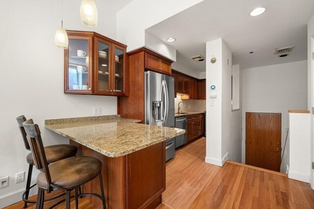 kitchen with appliances with stainless steel finishes, a sink, a peninsula, glass insert cabinets, and a breakfast bar