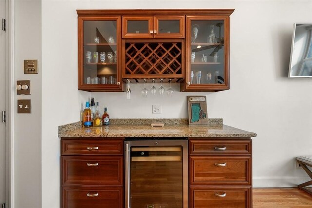 bar with baseboards, a bar, light wood finished floors, and beverage cooler