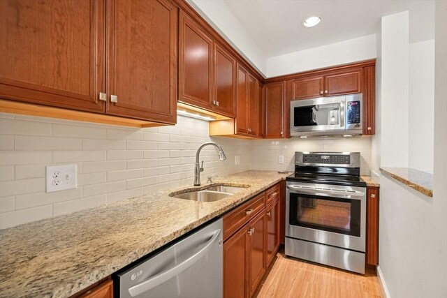 kitchen featuring appliances with stainless steel finishes, tasteful backsplash, a sink, light stone counters, and light wood-style floors