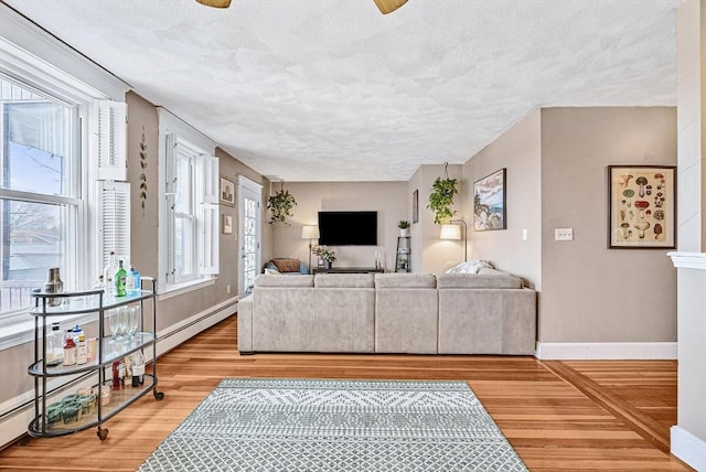 living room featuring a textured ceiling, light wood-type flooring, baseboards, and a baseboard heating unit