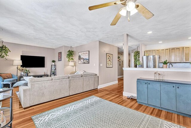 living room featuring baseboards, light wood-style floors, ceiling fan, recessed lighting, and a textured ceiling