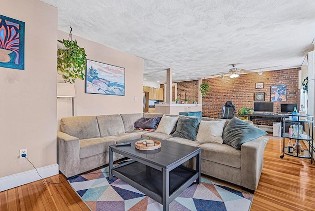 living room featuring a ceiling fan, light wood-style flooring, baseboards, brick wall, and a textured ceiling