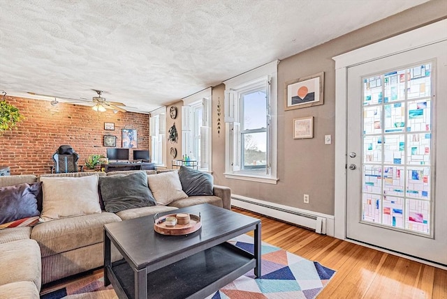 living room with a baseboard heating unit, wood finished floors, a textured ceiling, brick wall, and ceiling fan