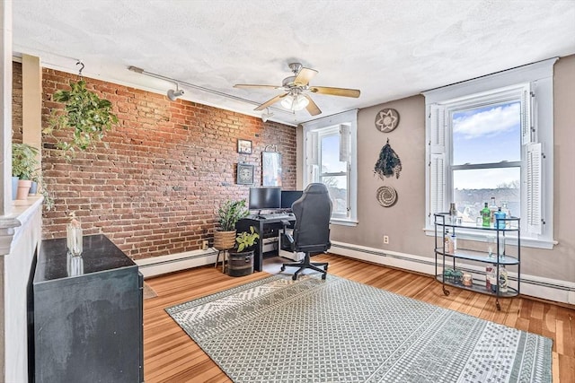 office space with brick wall, ceiling fan, wood finished floors, a textured ceiling, and baseboards