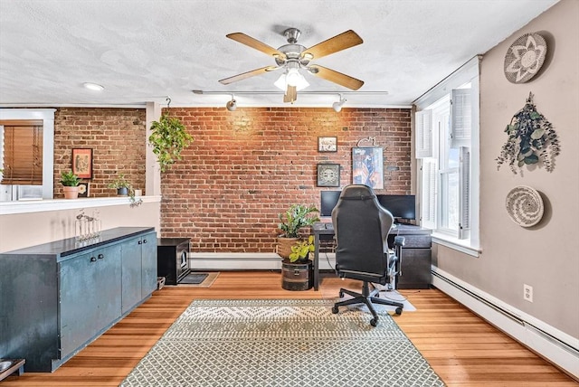 home office with a baseboard heating unit, brick wall, ceiling fan, light wood-style flooring, and baseboards