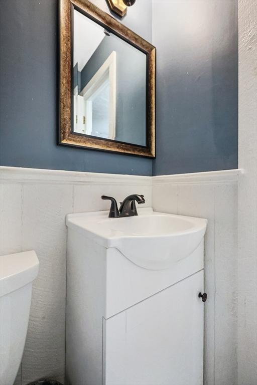 half bathroom with vanity, toilet, and a wainscoted wall