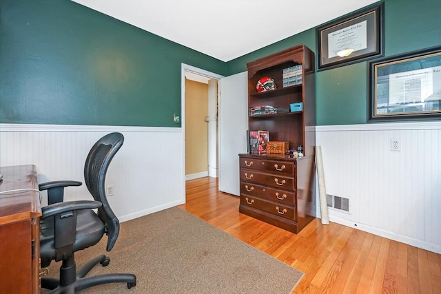 office featuring a wainscoted wall, visible vents, and wood finished floors
