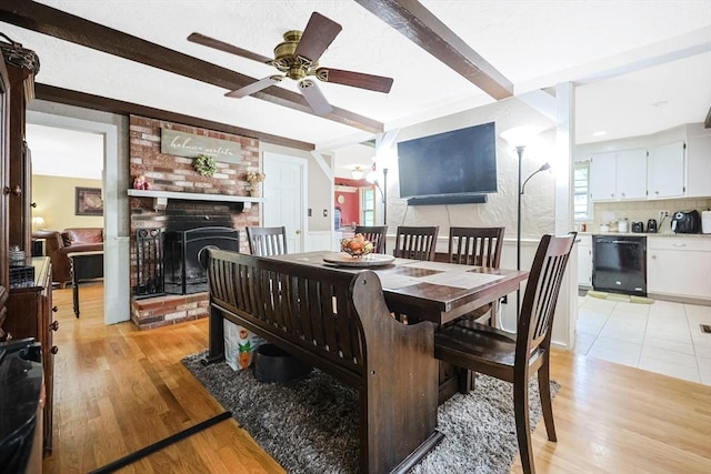 dining area with a fireplace, ceiling fan, beam ceiling, and light wood-style floors