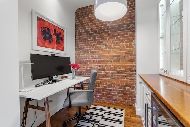 office area featuring baseboards, brick wall, light wood-style flooring, wine cooler, and an accent wall