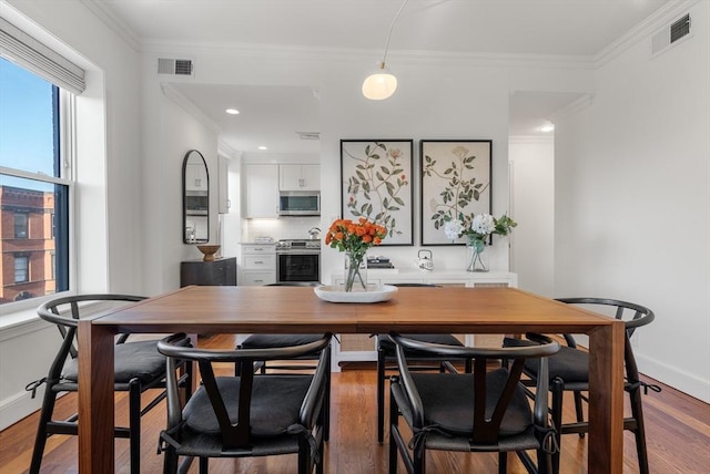 dining space featuring wood finished floors, visible vents, and ornamental molding